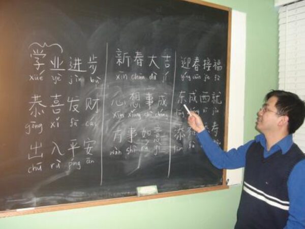 A man standing in front of a chalkboard with chinese characters written on it.