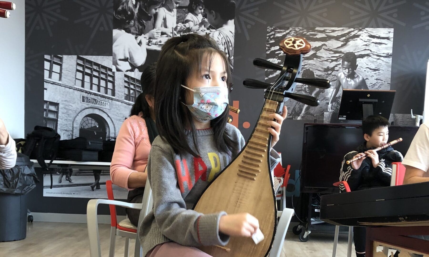 A little girl with a face mask playing an instrument.